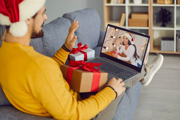 Young man sitting on couch with laptop and video calling his girlfriend on Christmas holidays - Photo, image