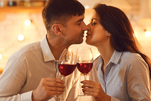 Молодая любящая пара целует друг друга и держит бокалы вина во время празднования Дня Святого Валентина - Фото, изображение