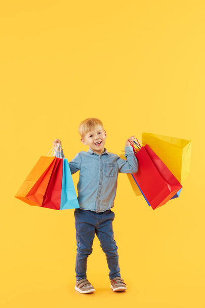 Sale of childrens products. Portrait of fun little child boy  on yellow background holding shopping bags, package. Looking at the camera. Banner. Space for text.  - Fotó, kép