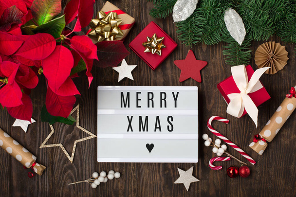 Buon Natale testo su Lightbox bianco con fiore rosso poinsettia, decorazioni natalizie, scatole regalo e bastoncini di zucchero su sfondo di legno scuro. Posa piatta, vista dall'alto, copiare spazio. Concetto regalo fatto a mano festivo - Foto, immagini