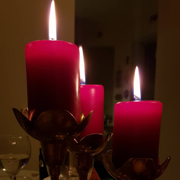 Κόκκινα κεριά διαφορετικού μεγέθους. Φωτιά υπό το φως των κεριών στην καύση wickes closeup. Φωτιά από κόκκινα κηροπήγια στο σκοτάδι - Φωτογραφία, εικόνα