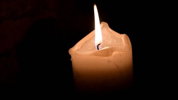 Soft focus to melted wax candle burning with dark background and copy space. Paraffin candle flame in darkness. Background of remembrance or Halloween celebration - Photo, Image