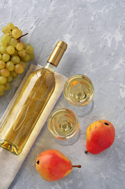 Dois copos com vinho, garrafa de vinho, pêras e escova de uvas em mesa cinza texturizada Vista superior. - Foto, Imagem