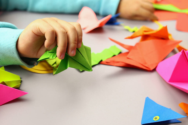Child makes origami crafts from colored paper, hands close-up - Photo, Image