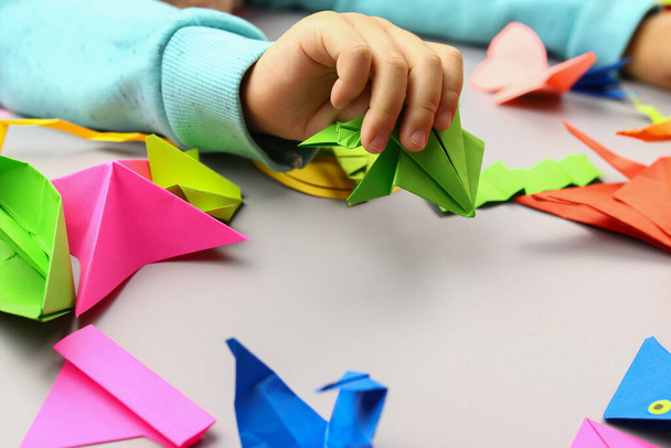 Child makes origami crafts from colored paper, hands close-up - Photo, Image
