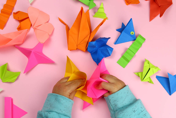 Dítě dělá origami z barevného papíru na růžovém pozadí - Fotografie, Obrázek