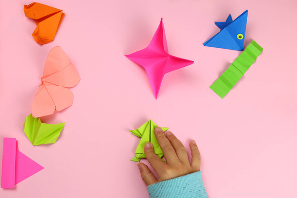 Dziecko robi origami od barwnego papieru na różowym tle - Zdjęcie, obraz