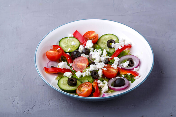 Light plate of Greek salad on a gray concrete background. - Fotó, kép