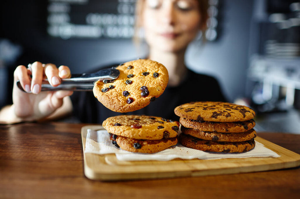 Barista holds tasty cookie at bar counter in coffee shop. Blurred image, selective focus - Photo, image
