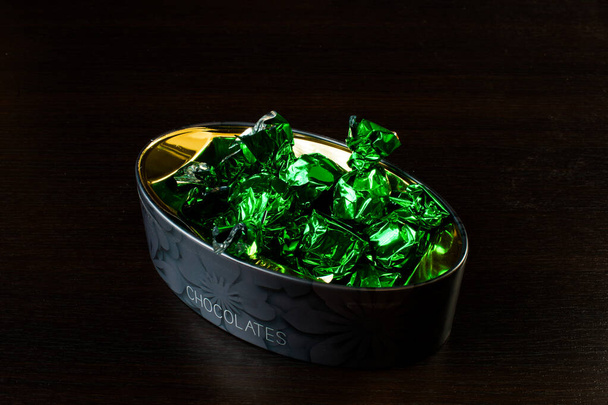 caixa com doces em papel alumínio verde sobre um fundo preto - Foto, Imagem
