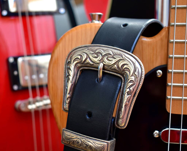 Gitary elektryczne i skórzany pasek ze srebrną klamrą z bliska. - Zdjęcie, obraz