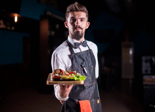 Young waiter helpfully serves dish in the restaurant. - Photo, Image