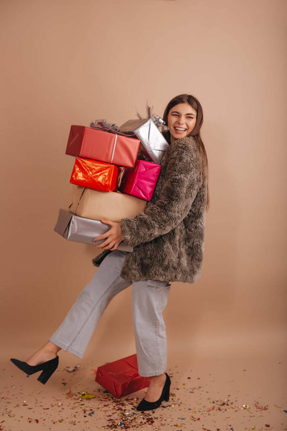 Дівчина з коротким хутряним пальто, що рухається з багатьма подарунковими коробками в руках ізольовані на бежевому фоні
. - Фото, зображення