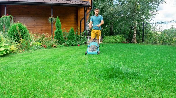 A man takes care of the lawn with a lawn mower. Regular mowing of the grass in the summer season. A man mows the grass with an electric lawn mower. - Photo, Image