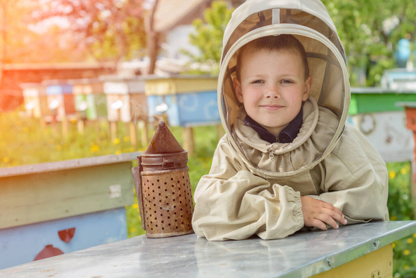 Chłopiec w ochronnym ubraniu pszczelarz pracuje w pasiece. Pszczelarstwo - Zdjęcie, obraz