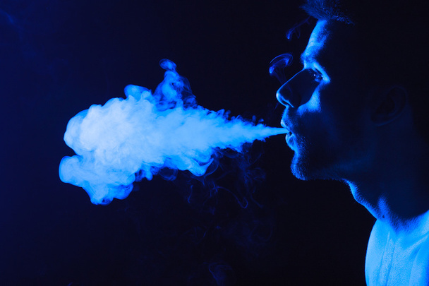 donker en nors shot van een jonge man roken op een zwarte achtergrond - Foto, afbeelding
