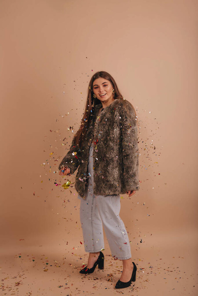 Cheerful smiling girl standing under confetti rain over a beige background.  - Photo, image