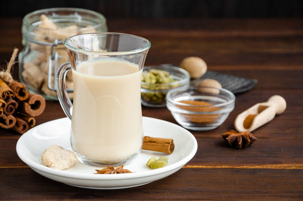 Ζεστό τσάι με γάλα, κανέλα, κάρδαμο, γλυκάνισο και άλλα μπαχαρικά, ινδική masala τσάι σε ένα γυάλινο κύπελλο σε ξύλινο φόντο. αντίγραφο χώρου - Φωτογραφία, εικόνα