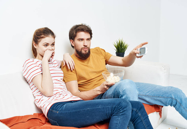 interested woman and bearded man sit on the couch popcorn in a plate and flower in a pot - Foto, imagen