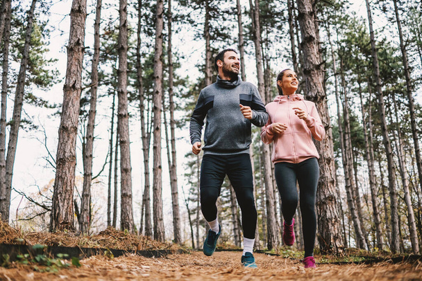 Longitud completa de la pareja en forma corriendo por los bosques en otoño y preparándose para la maratón. - Foto, imagen