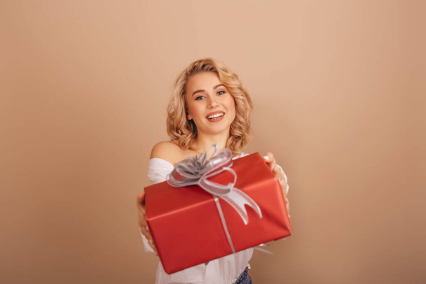Щаслива молода жінка, посміхаючись у білій блузці, дарує різдвяну подарункову коробку ізольований бежевий фон. Копіювати пробіл
. - Фото, зображення