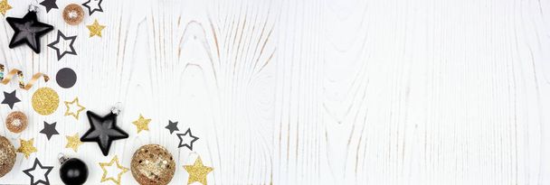 Fin de año borde de esquina víspera de oro y confeti negro estrellas, decoraciones y serpentinas. Vista superior sobre un fondo de madera blanca. - Foto, imagen