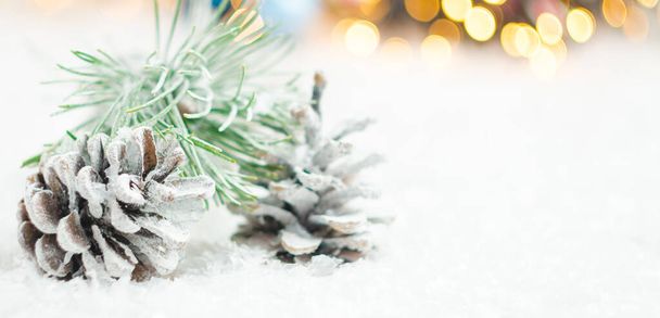 Pine cones and spruce branch covered with snow on the background of blurred lights of garland. Christmas concept with copy space. - Photo, image