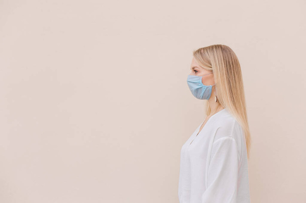 Photo beautiful young woman wearing a face mask to protect the virus isolated on an beige background.Copy space. - Фото, зображення