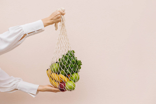 Reusable eco bag for shopping. String shopping bag with fruits in the hands of a young woman. Zero waste, plastic free concept. Eco lifestyle. Eco shopping. Conscious consumption. Eco trend.Copy space - 写真・画像