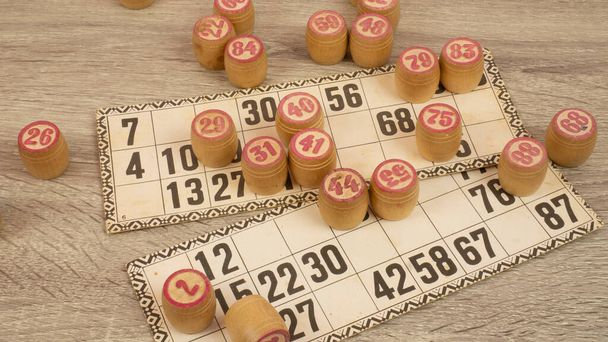 Table game Bingo. Wooden Lotto barrels, playing cards for Lotto game with black bag on a wooden light table - Photo, Image