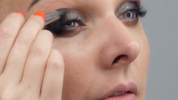 Een mooie spectaculaire jonge vrouw in brengt make-up op haar gezicht met een speciale borstel voor een spiegel - Video