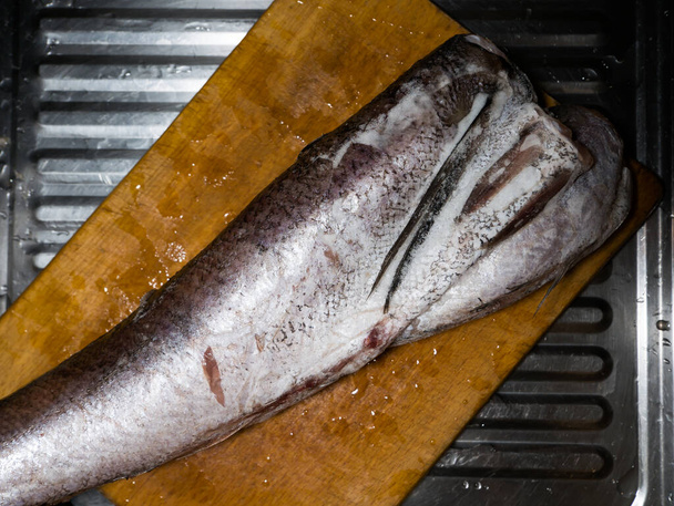 Pescado de merluza grande congelado se encuentra en el tablero de la cocina - Foto, Imagen