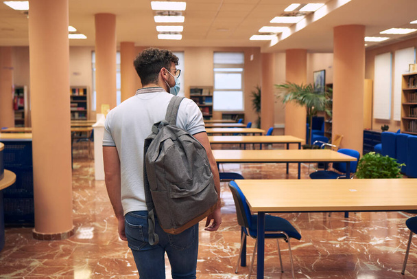 Boy with mask and backpack enters an empty library - Photo, Image