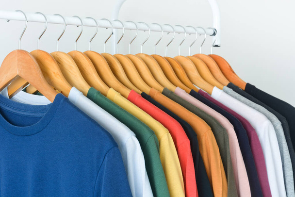 close up collection of colorful t-shirts hanging on wooden clothes hanger in closet or clothing rack over white background - Foto, Imagem