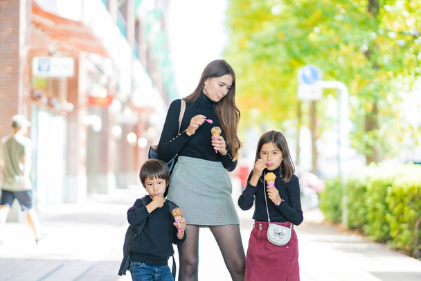 Äiti ja kaksi lasta syö jäätelöä hymyillen ulkona - Valokuva, kuva