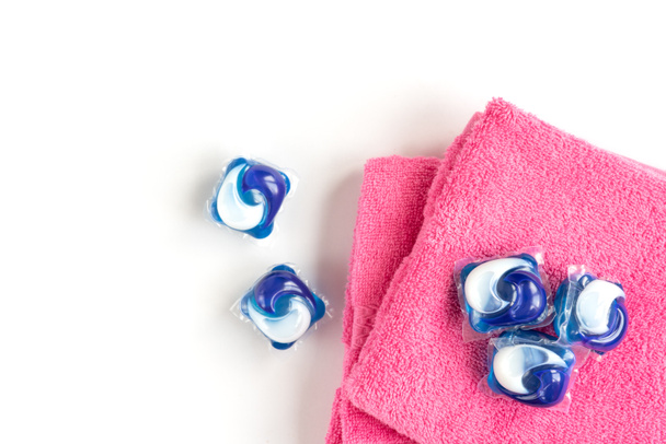 白い背景に隔離された洗剤カプセルポッドとピンクのタオルを洗う. - 写真・画像