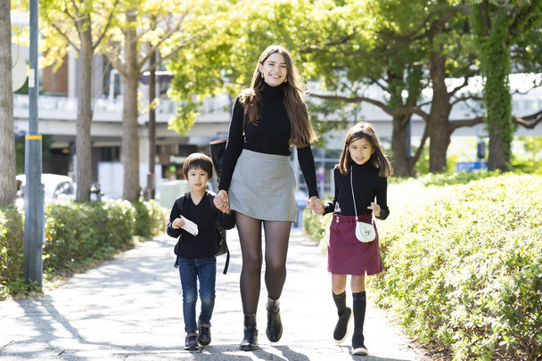 Mother and two children walking outdoors holding hands with smile - Foto, imagen