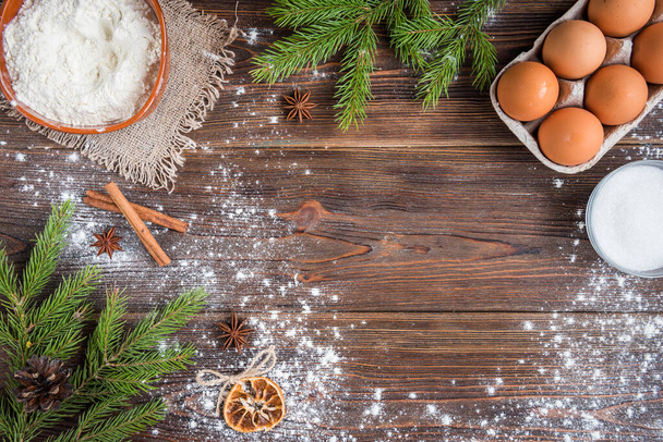 Ingredients for cooking christmas baking. Flour, eggs, sugar and spices on dark wooden background with fir branches. - Zdjęcie, obraz
