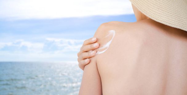 Zeevrouw concept. close-up vrouw toepassen zonnebrandcrème op wazig beeld van de blauwe zee en de blauwe lucht. voor bescherming UV A, UV B - Foto, afbeelding