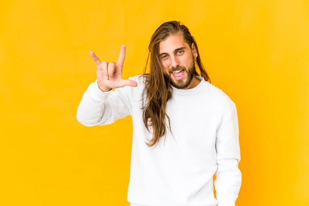 Young man with long hair look showing a horns gesture as a revolution concept. - Photo, Image