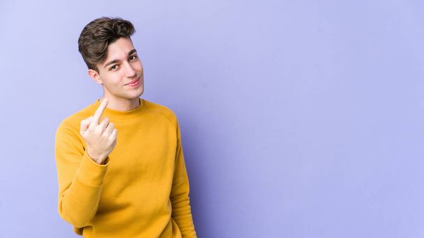 Junger kaukasischer Mann isoliert auf violettem Hintergrund und zeigt mit dem Finger auf dich, als würde er dich einladen, näher zu kommen. - Foto, Bild