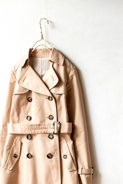 Beige trench coat isolated hanging on a hanger in a white wall. Close up and copy space. - Foto, immagini