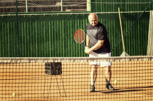 A middle-aged man plays tennis on the court. Activity and movement. - Φωτογραφία, εικόνα