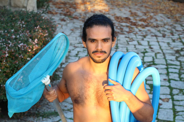 zblízka portrét pohledného mladého muže s knírem a dlouhými vlasy držící síť a dýmku pro čištění bazénu - Fotografie, Obrázek