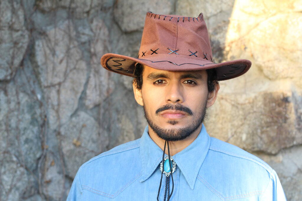 zblízka portrét pohledného mladého muže s knírem v kovbojském klobouku před kamennou zdí - Fotografie, Obrázek