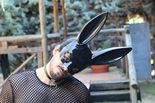крупным планом портрет красивого молодого человека в чистой рубашке и черной маске кролика на открытом воздухе - Фото, изображение