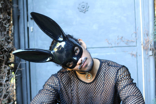 крупным планом портрет красивого молодого человека в чистой рубашке и черной маске кролика на открытом воздухе - Фото, изображение