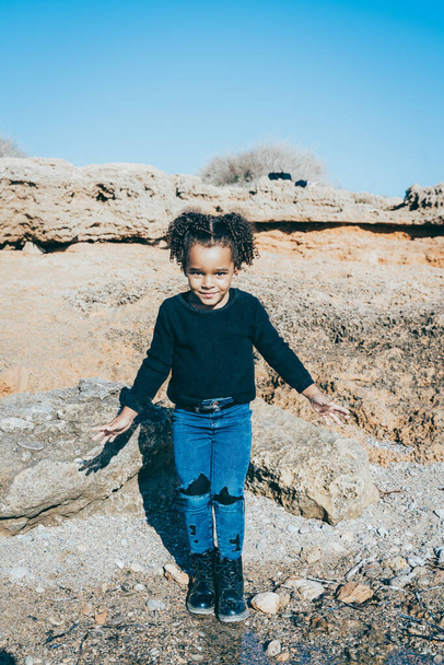 Афроамериканка, одетая в городскую одежду, счастливо позирует и веселится в скалистой естественной бухте - Фото, изображение