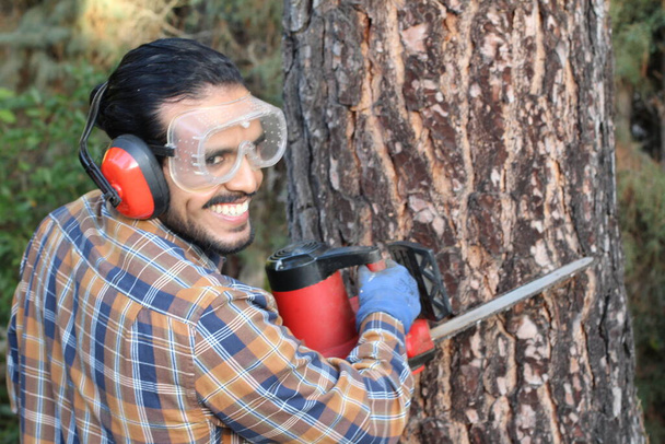 Nahaufnahme Porträt eines gutaussehenden jungen Mannes mit Schnurrbart, der Holzfäller mit Sägemaschine arbeitet - Foto, Bild