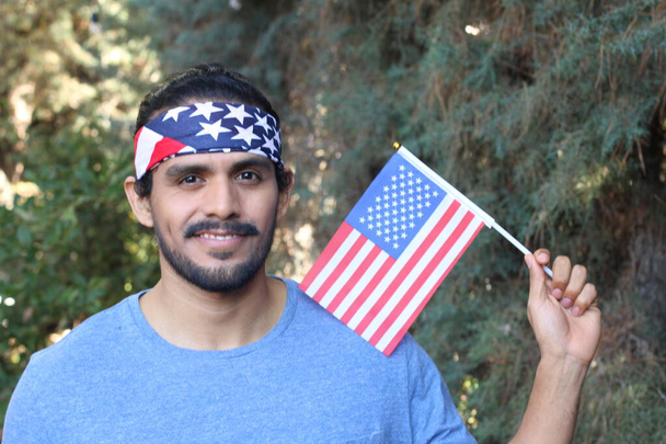 portret van knappe jongeman met Amerikaanse vlag en hoofdband in park - Foto, afbeelding